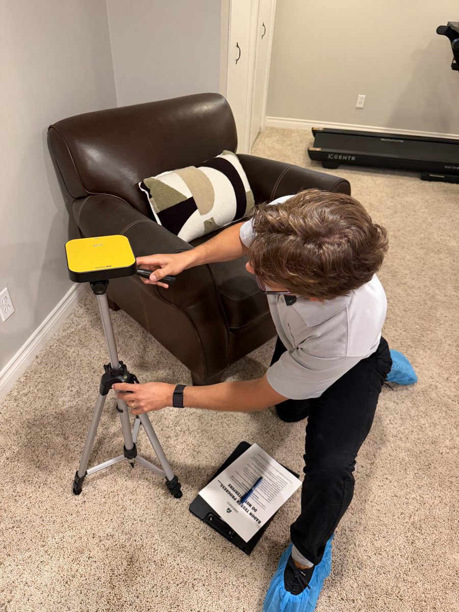 Hunter setting up a continuous radon monitor on a tripod in a home basement